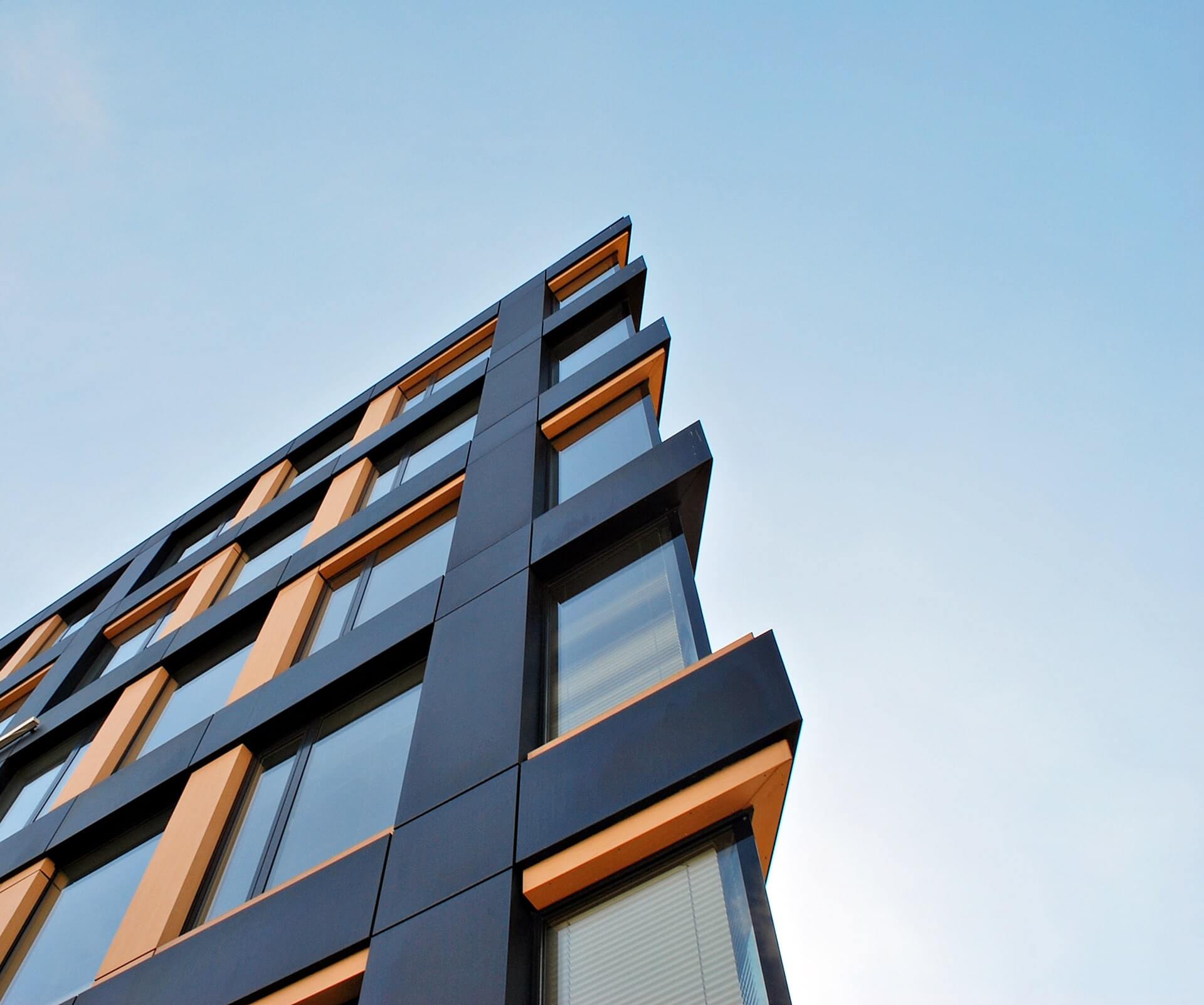 Modern building facade with black and orange panels against a clear blue sky.