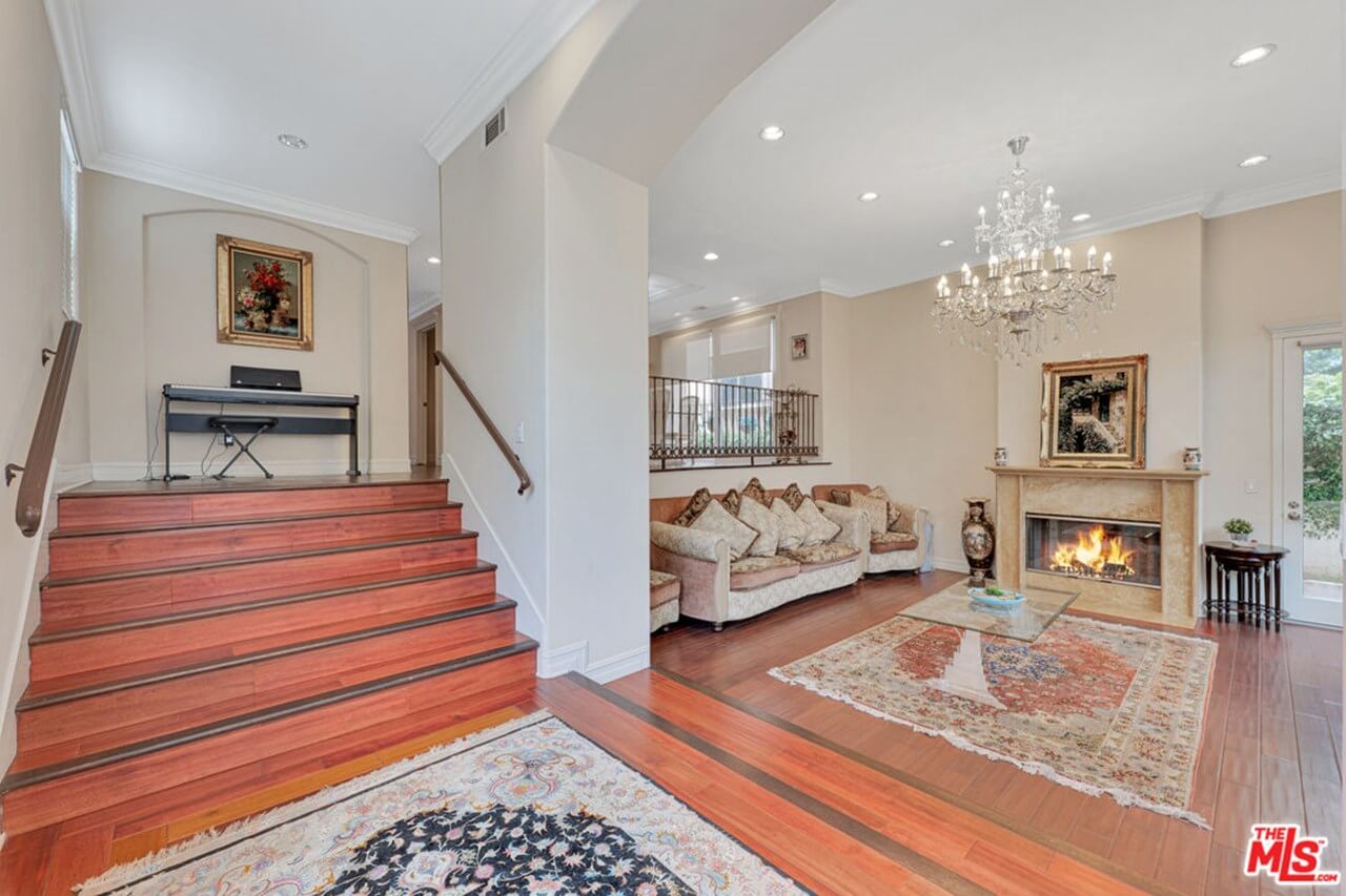 Elegant living room with fireplace, chandelier, and piano on raised platform.