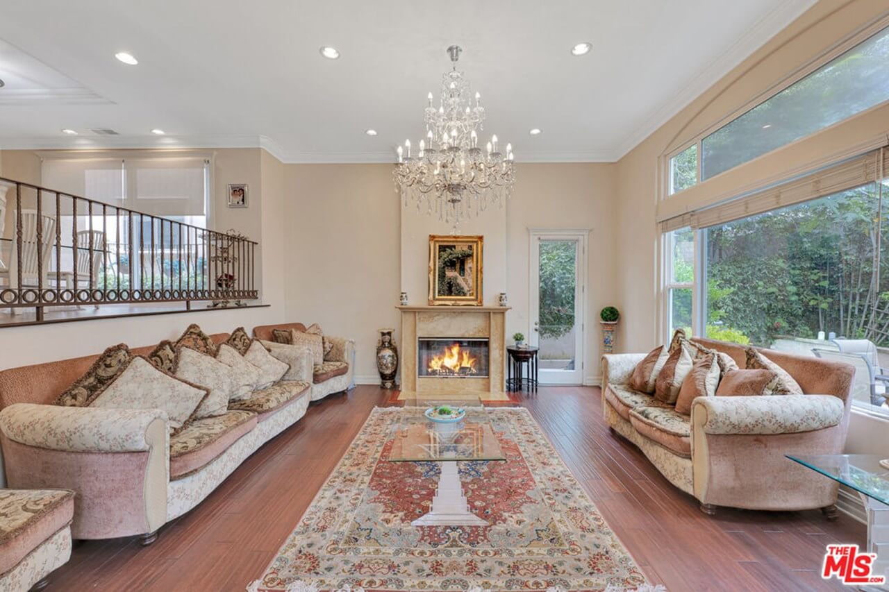 Elegant living room with a chandelier, fireplace, and large windows overlooking greenery.
