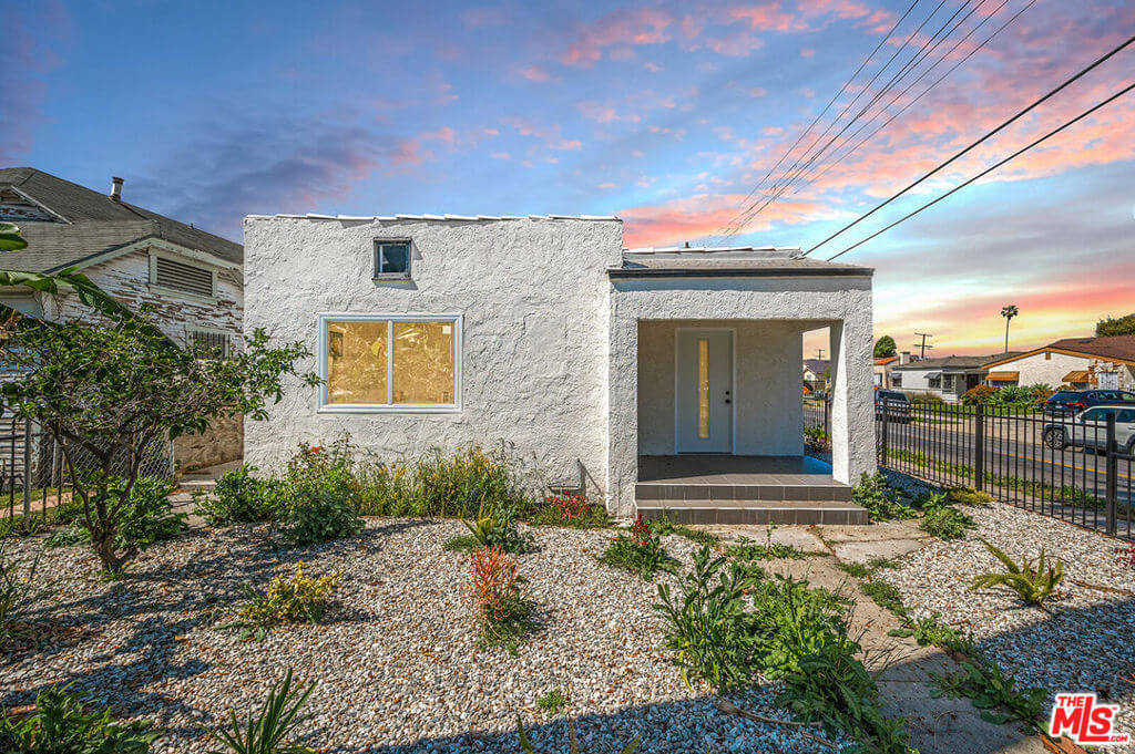 Small white stucco house with gravel yard and a colorful sunset sky.