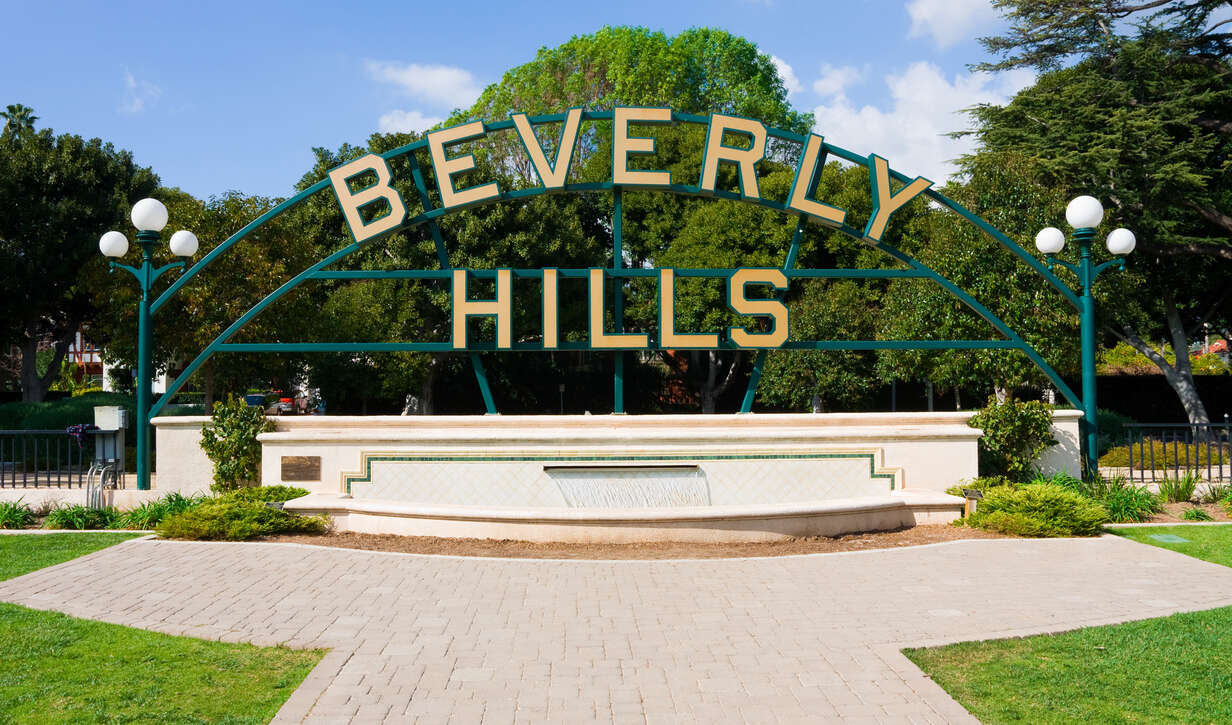 Beverly Hills sign against a clear blue sky with greenery.