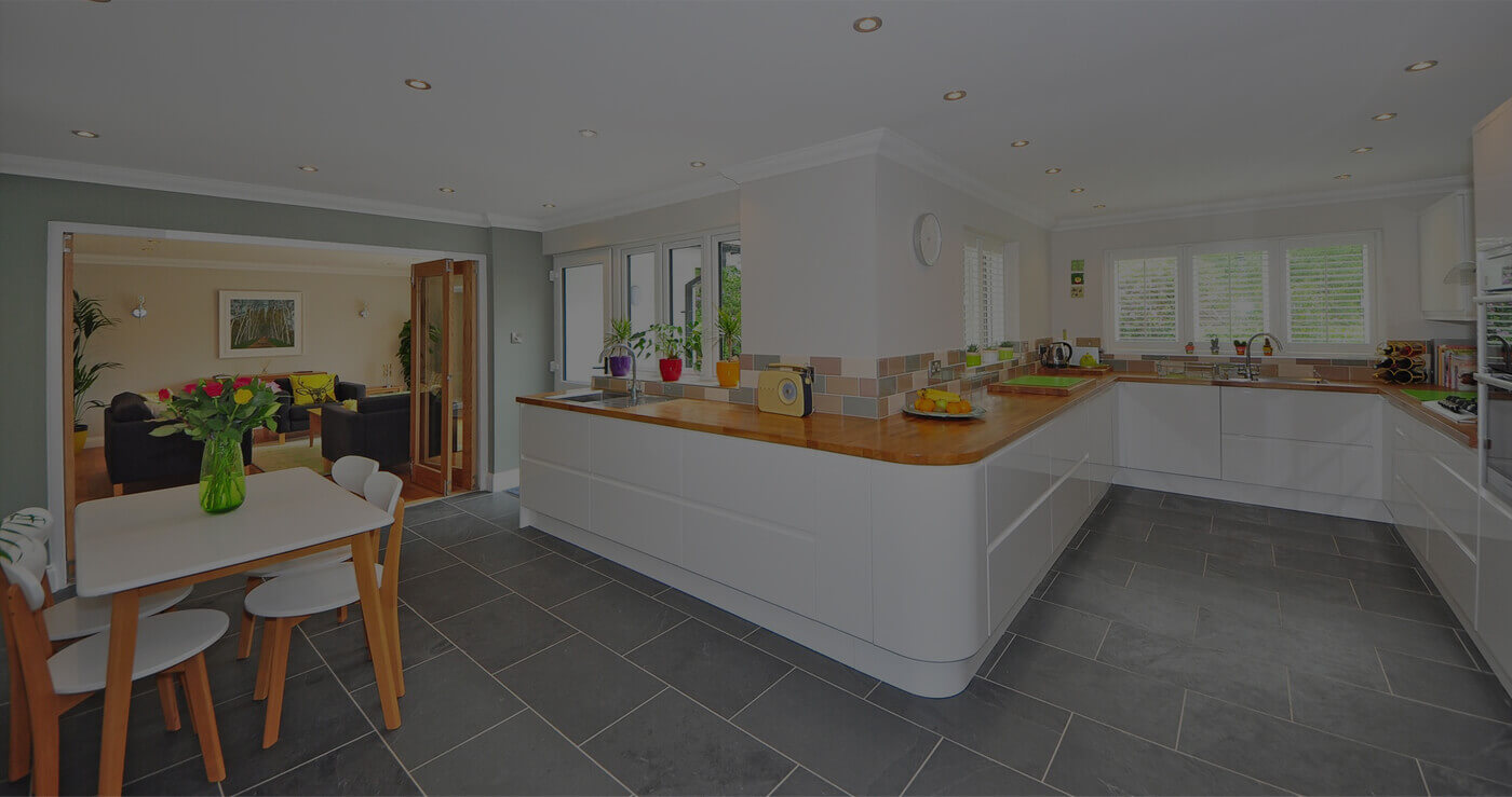 Modern kitchen with white cabinets and wooden countertops, adjacent to a dining area with a flower vase.