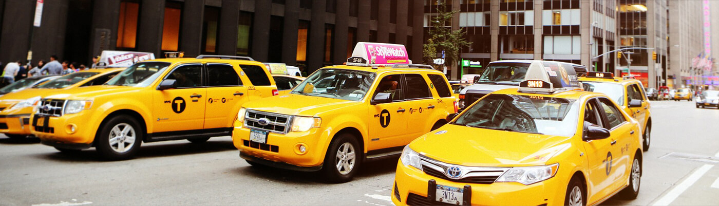 Line of yellow taxis waiting on a city street.