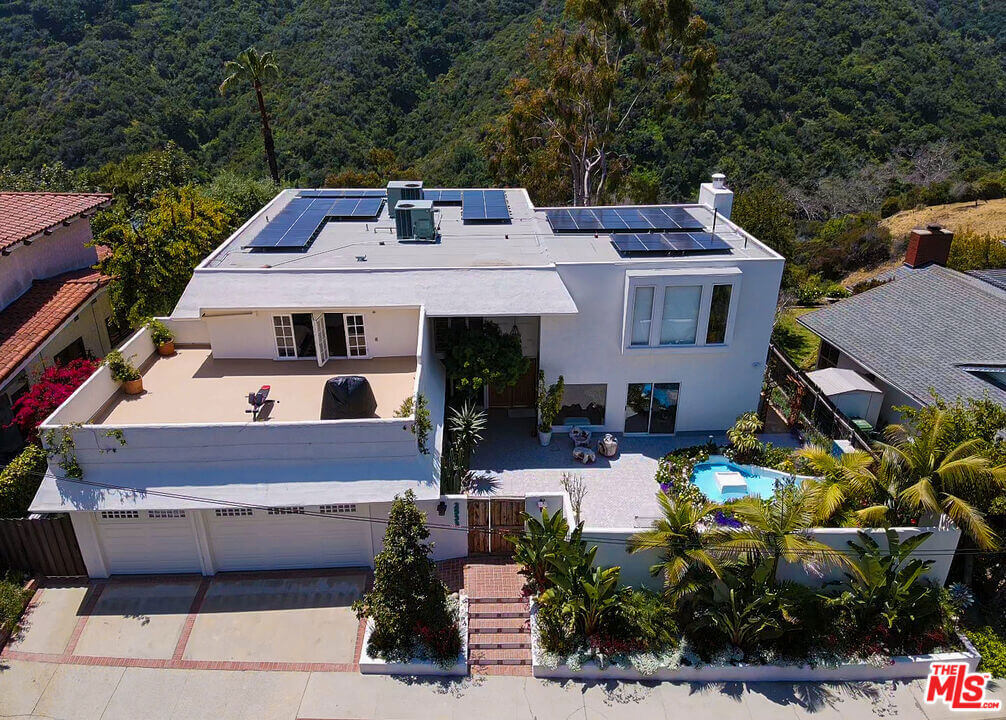 Modern white house with solar panels, rooftop terrace, and small pool surrounded by greenery.