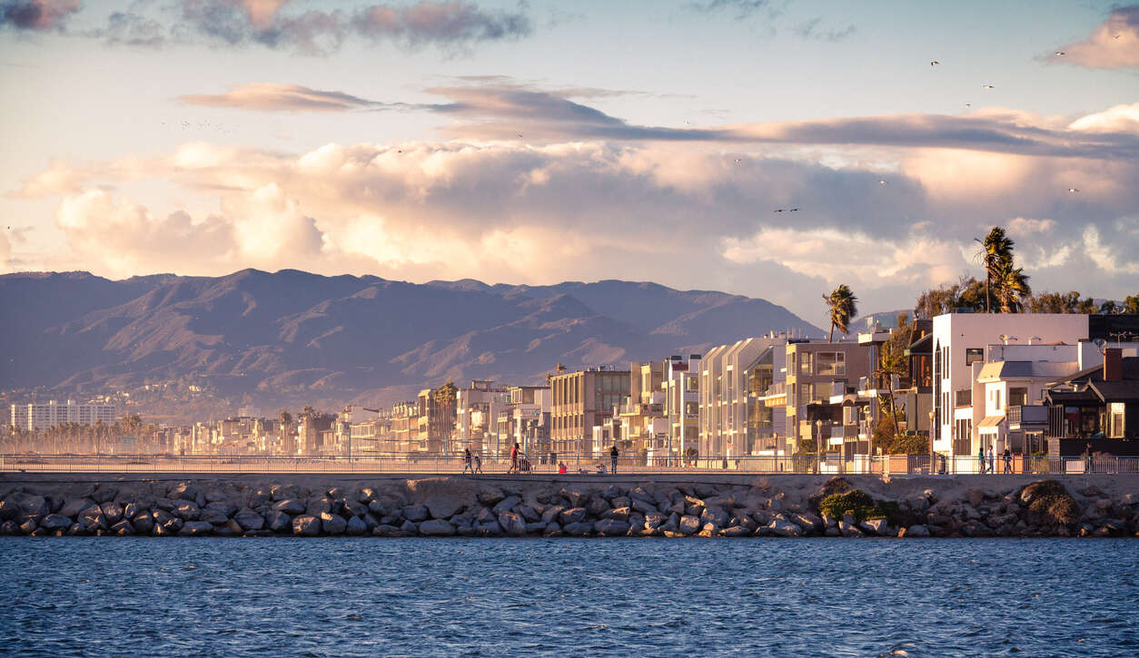 City skyline with mountains and ocean under a cloudy sky.