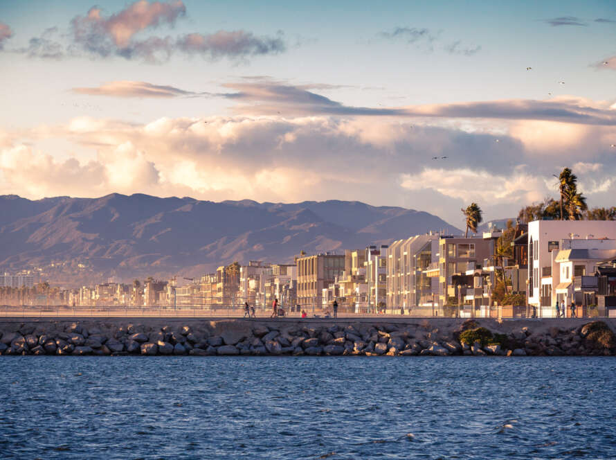 City skyline with mountains and ocean under a cloudy sky.
